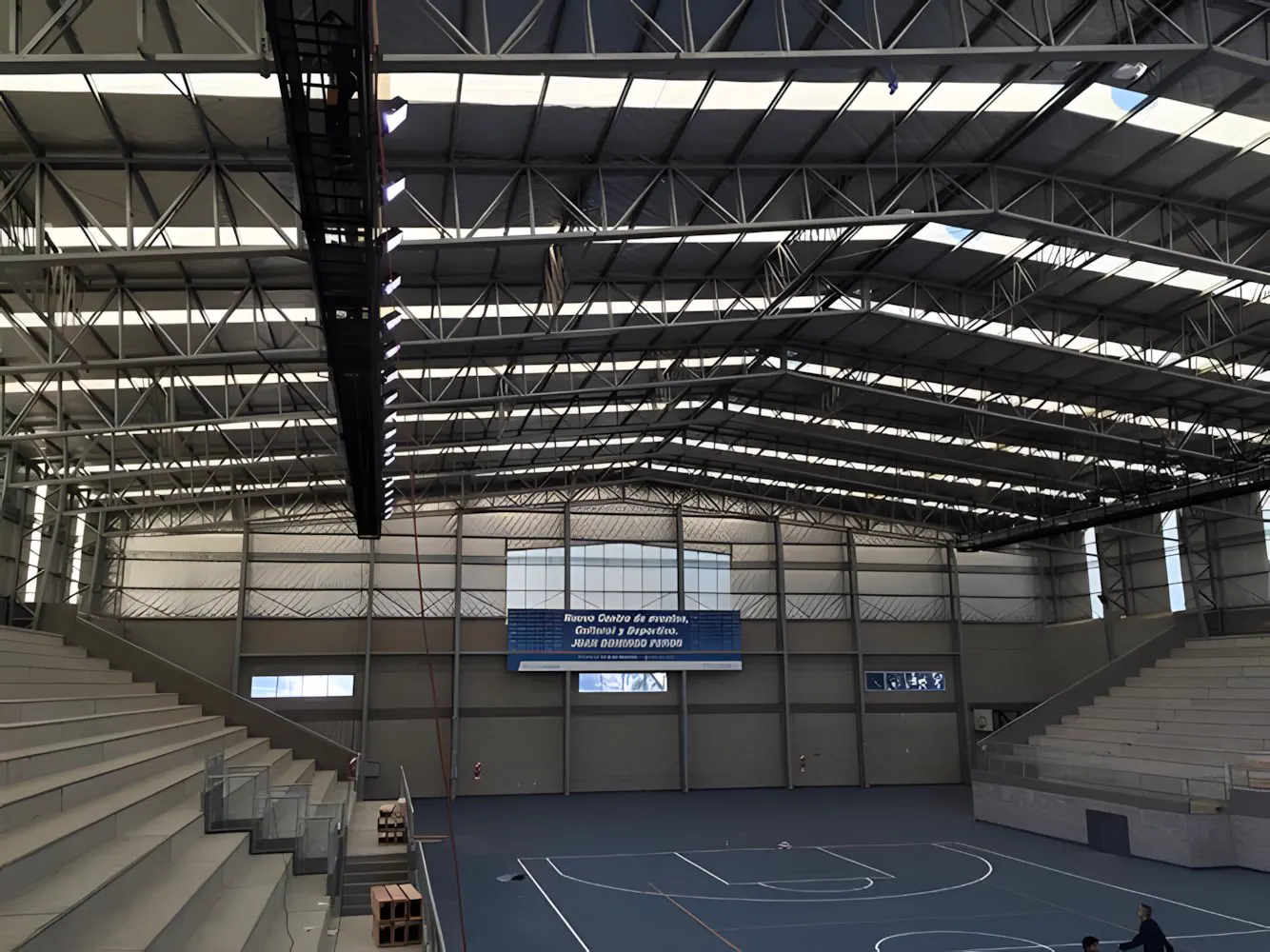 Interior del polideportivo visto desde la tribuna, con la cancha y el techo de estructura metálica