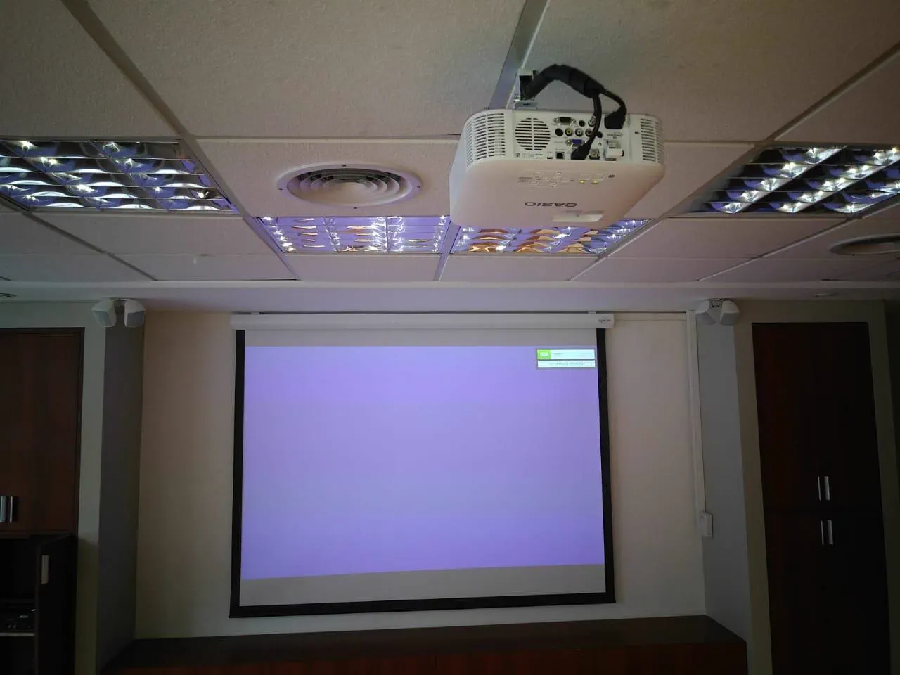 La sala de reuniones con la pantalla motorizada bajada y el proyector encendido