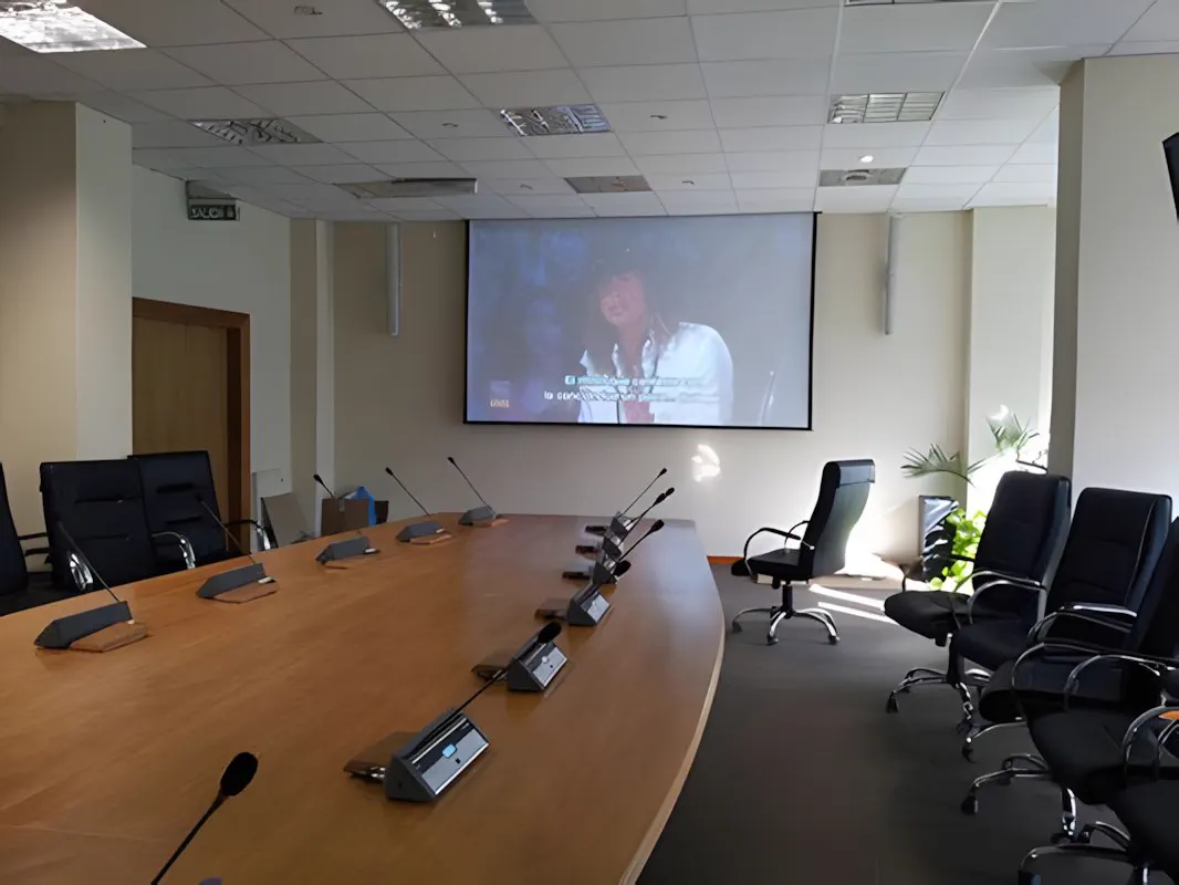 Sala de reuniones con el monitor de videoconferencia y los micrófonos de mesa