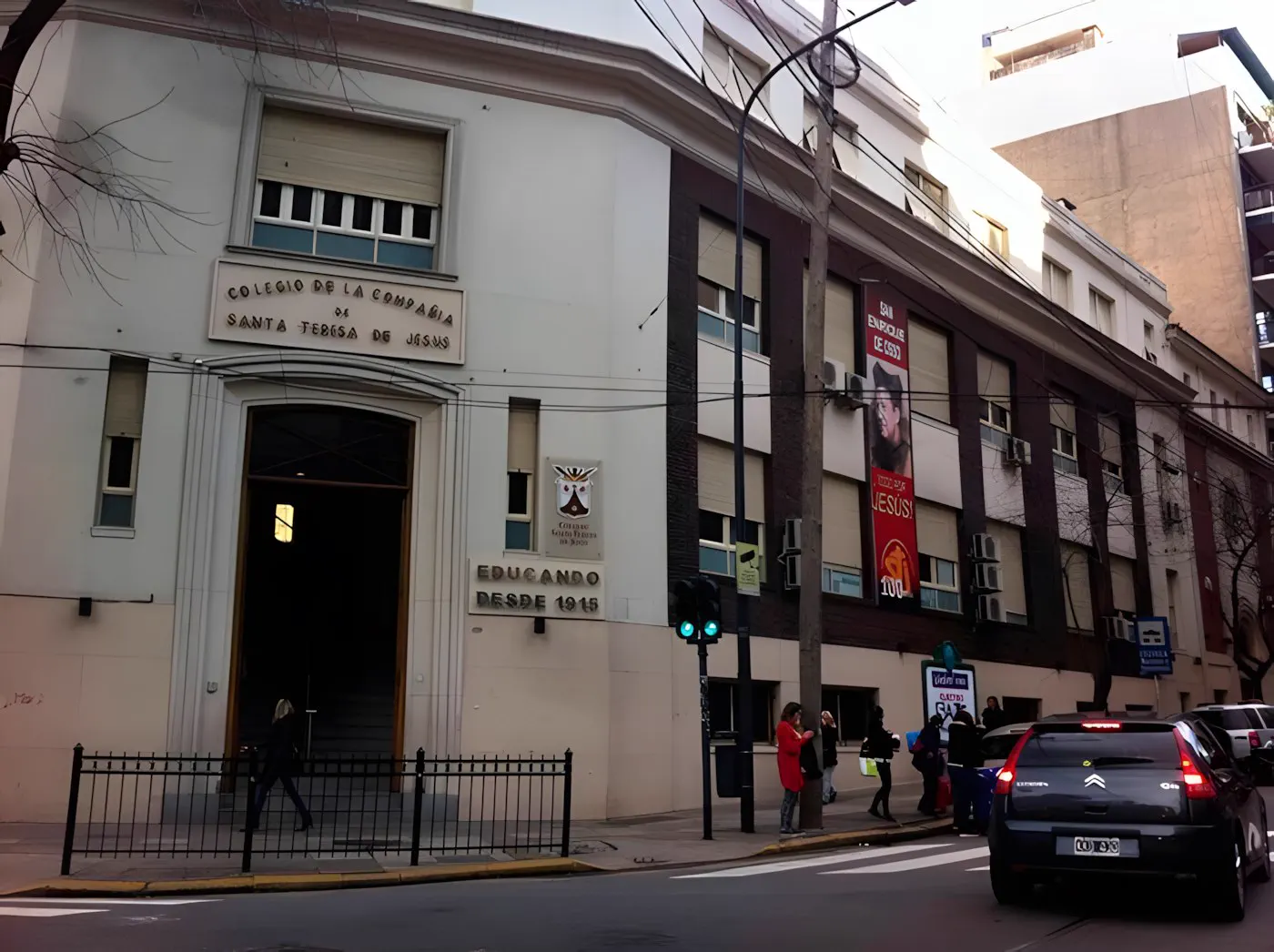 Frente del colegio sobre la vereda, con la entrada y el cartel de la escuela