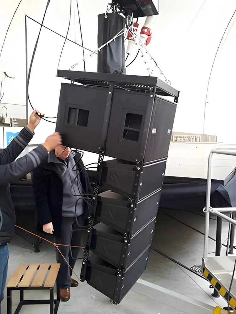 El line array siendo izado, con un técnico armando los módulos