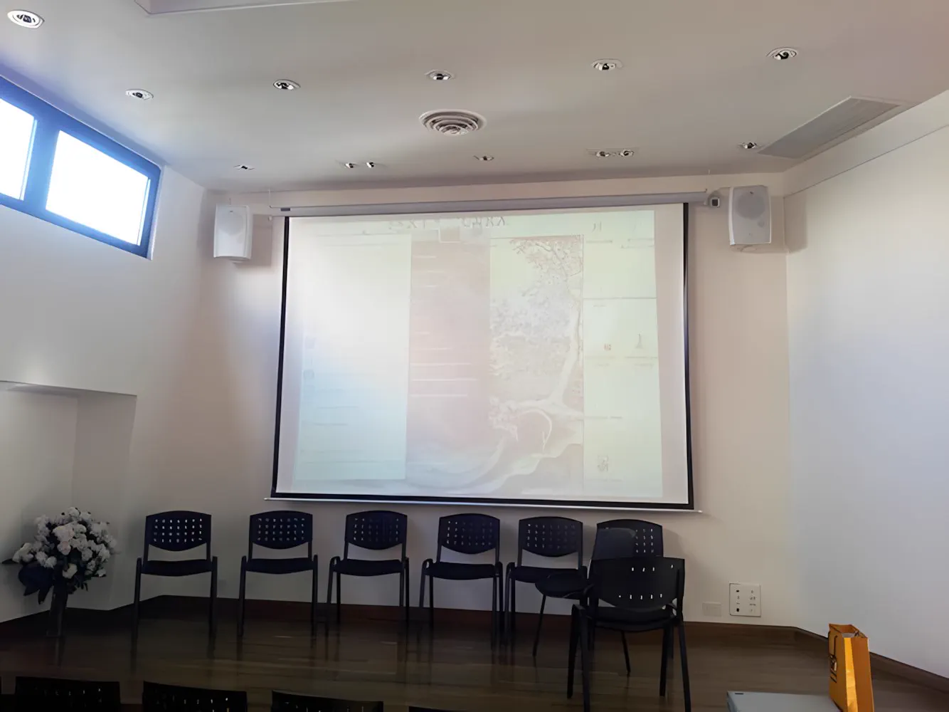 Salón auditorio con pantalla de proyección y parlantes de dos vías a los costados