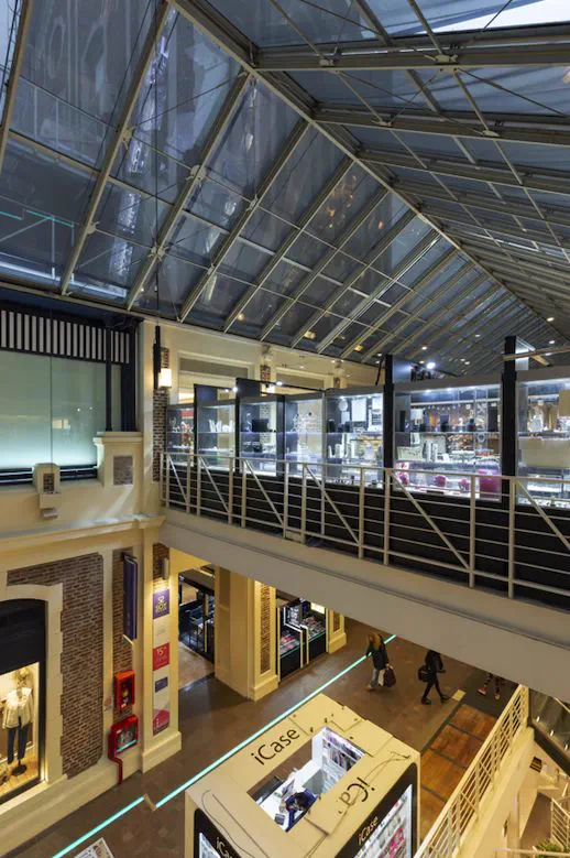 Interior de un shopping de dos niveles con techo vidriado y locales iluminados
