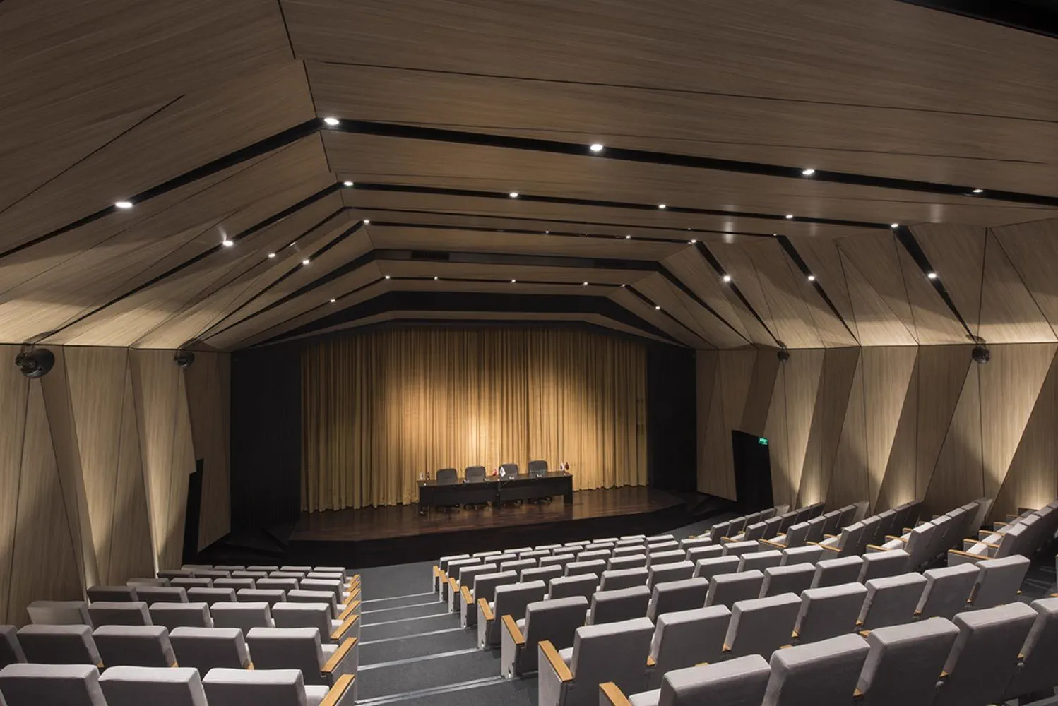 Auditorio revestido en madera con butacas, escenario y mesa de panel con micrófonos